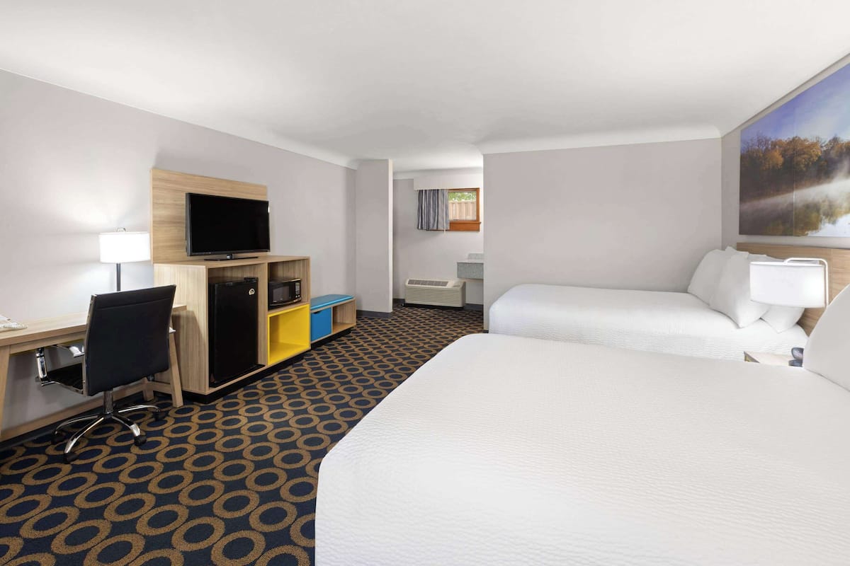 A hotel room with a large bed, a desk with a computer, a TV, and a small kitchenette.