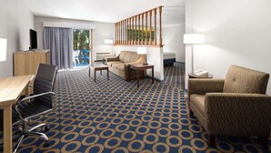 A hotel room with a blue patterned carpet, a wooden desk with a chair, a sofa, a small table, a lamp, and a staircase with a railing. - Days Inn by Wyndham Wauseon (Wauseon)