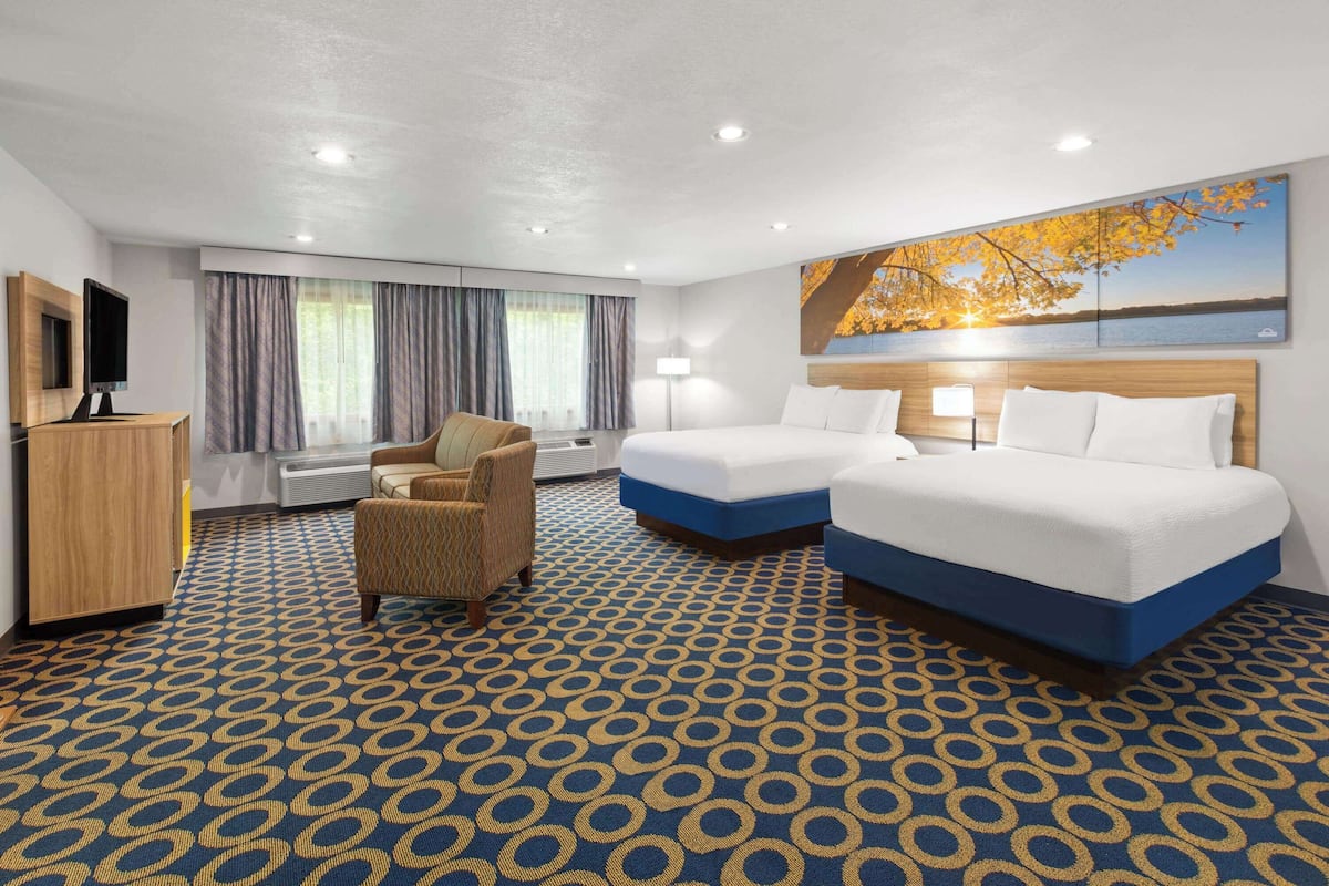 A hotel room with two beds, a TV, a desk, a chair, and a large window with curtains.