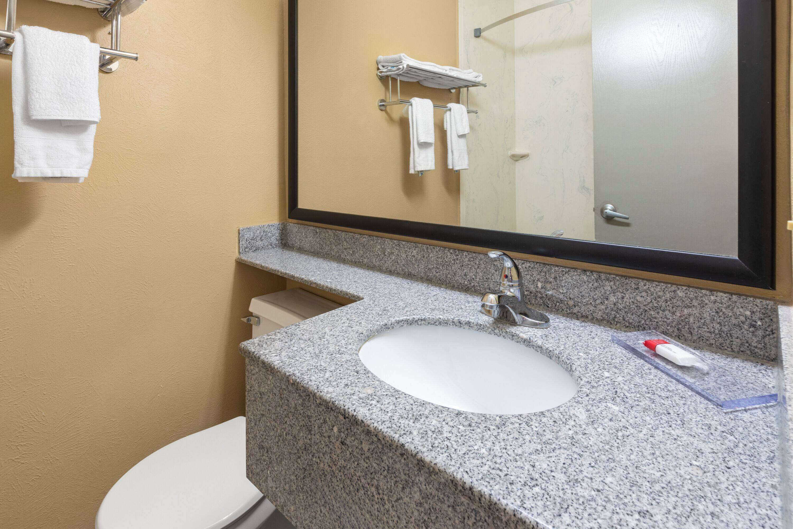 A bathroom with a granite countertop sink, a mirror, and a toilet.