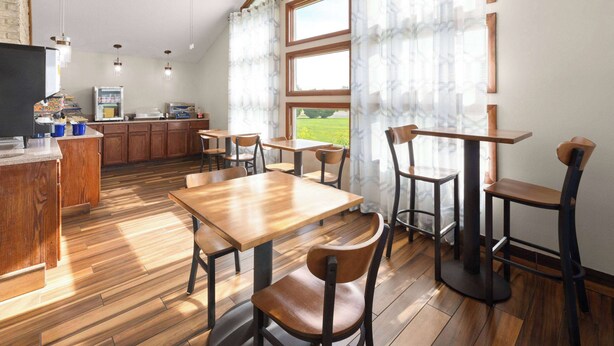 A restaurant with wooden tables and chairs, a kitchen area, and large windows with curtains. - Days Inn by Wyndham Wauseon (Wauseon)