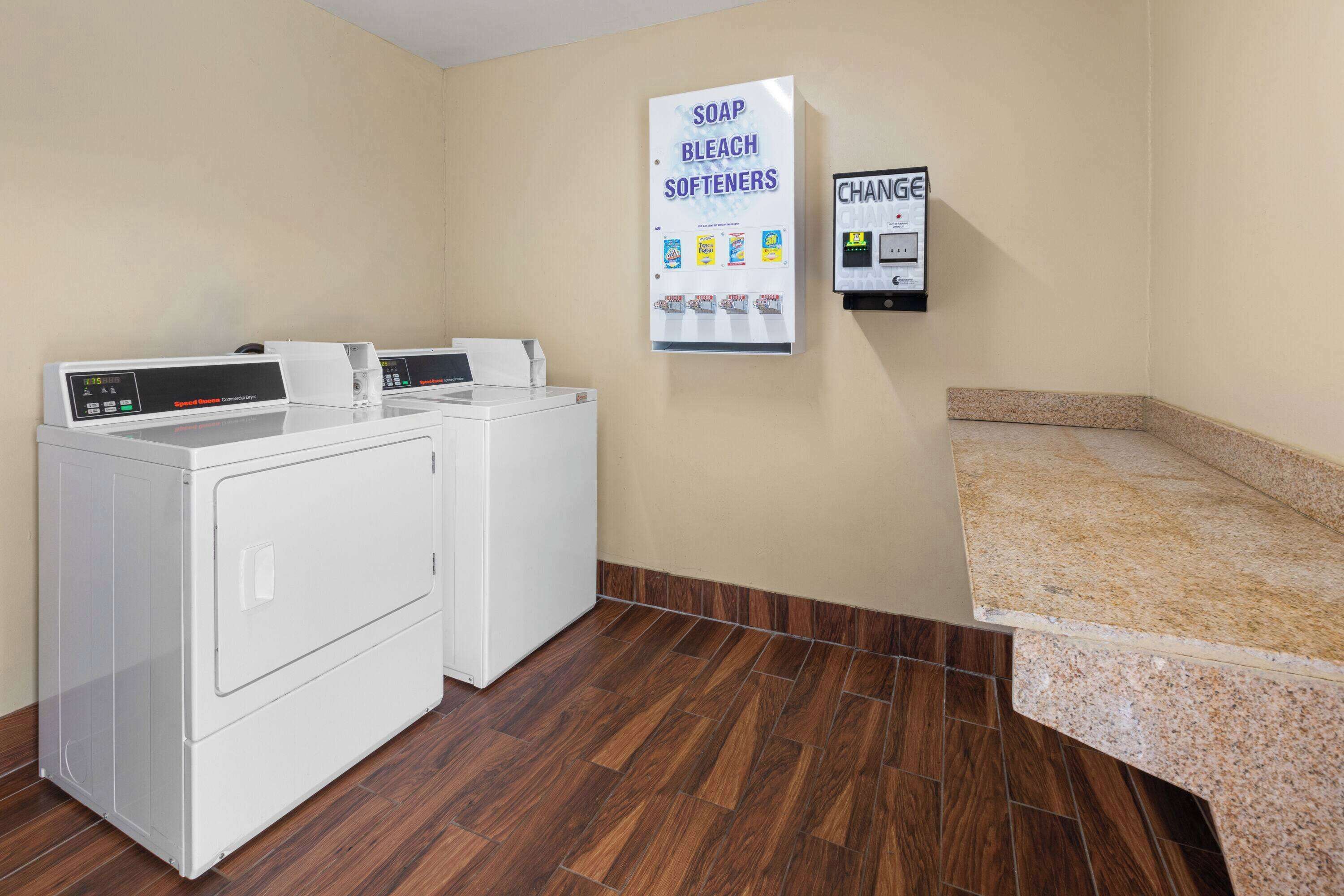 A laundry area with two washing machines, a wall-mounted soap and bleach dispenser, and a change machine.