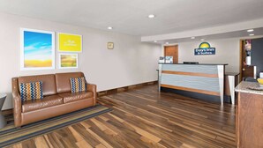 A reception area with a brown leather sofa, a reception desk, and framed pictures on the wall. - Days Inn by Wyndham Wauseon (Wauseon)