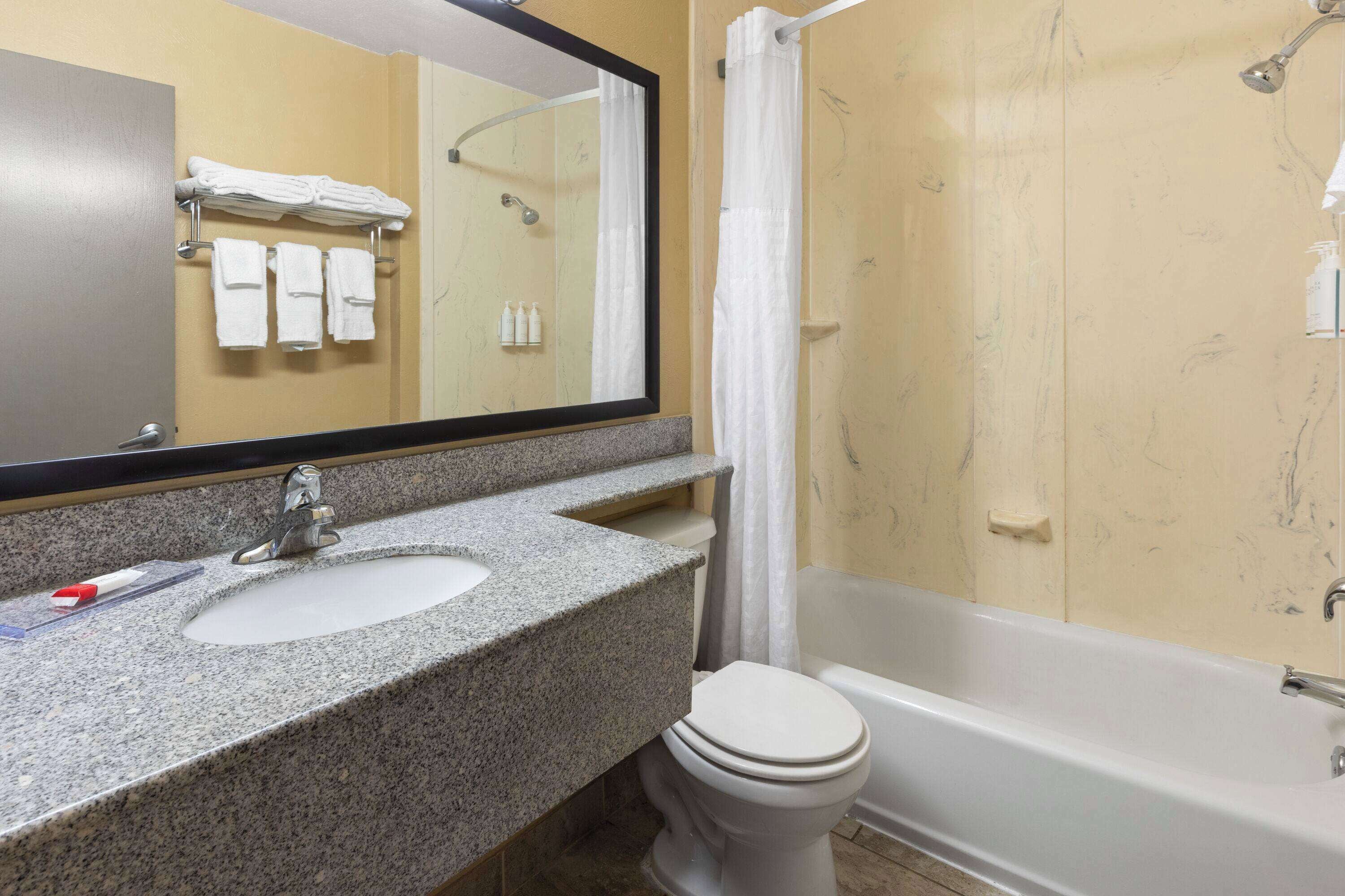 A bathroom with a granite sink, a white toilet, a bathtub, and a mirror.