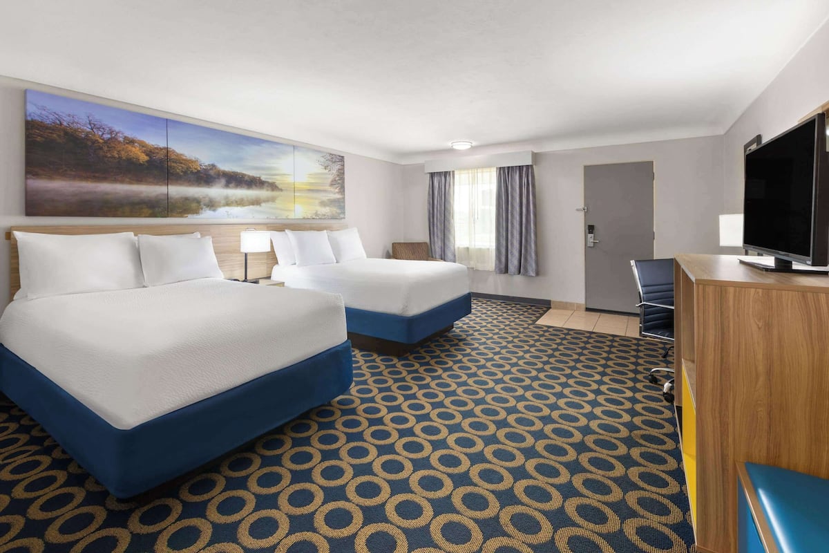 A hotel room with two beds, a television, a desk, and a large window with curtains.