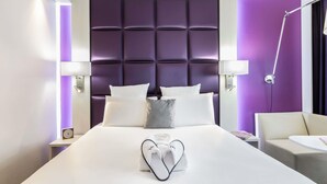 Een moderne hotelkamer met een groot bed, een hoofdeinde met een gestoffeerd ontwerp, twee bedlampen, een nachtkastje met een klok en een stoel.