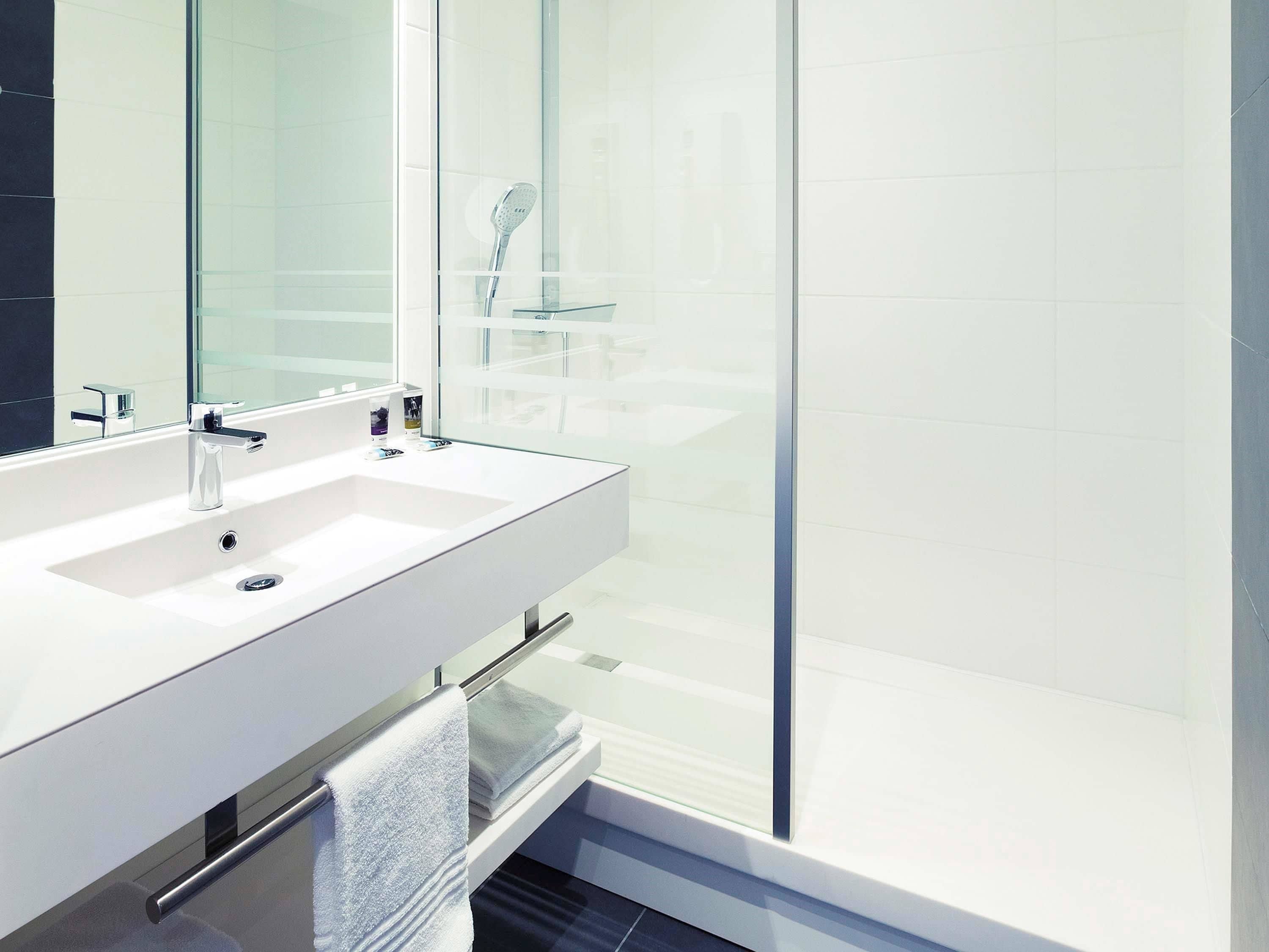 Un baño moderno con un lavabo blanco, una cabina de ducha de vidrio y un cabezal de ducha visible.