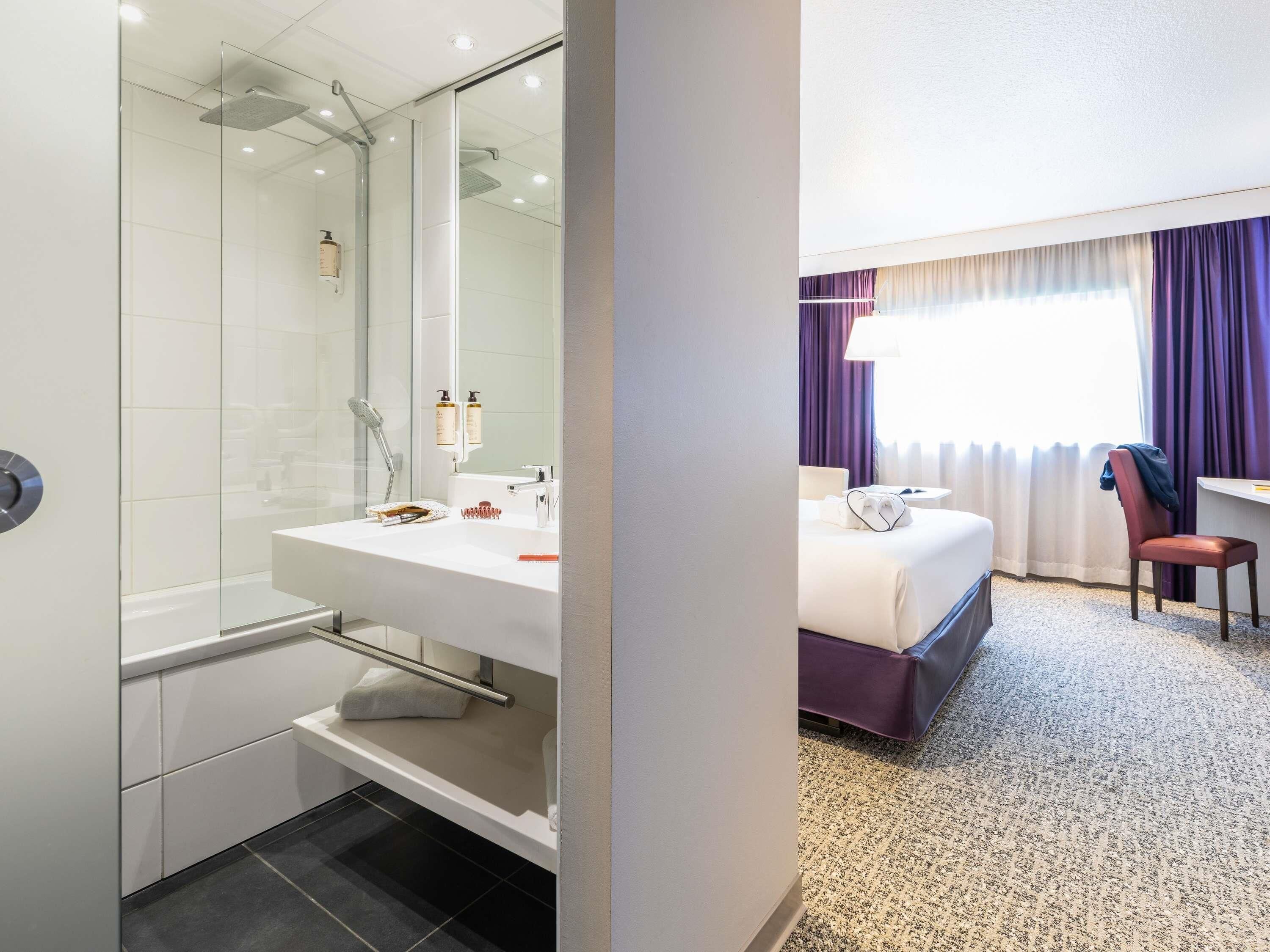 Habitación de hotel con ducha, lavamanos, cama, silla y escritorio.