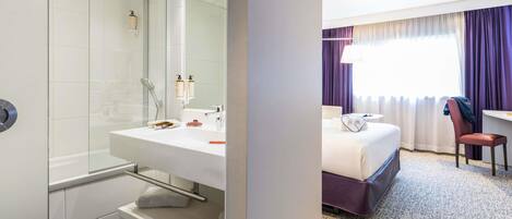 Habitación de hotel con ducha, lavamanos, cama, silla y escritorio.