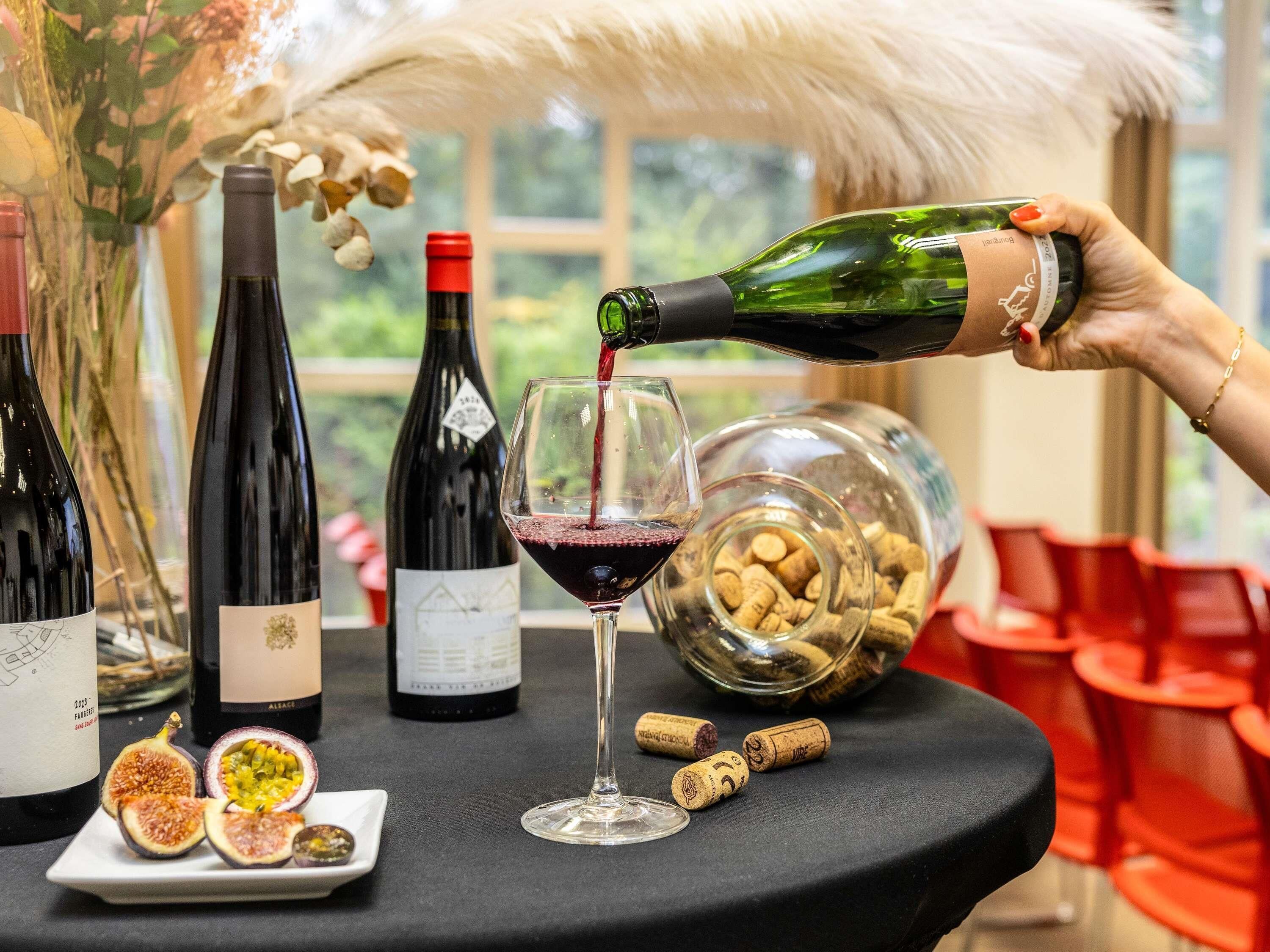 Une table avec des bouteilles de vin, un verre de vin rouge et une bouteille de champagne dont on verse le contenu.