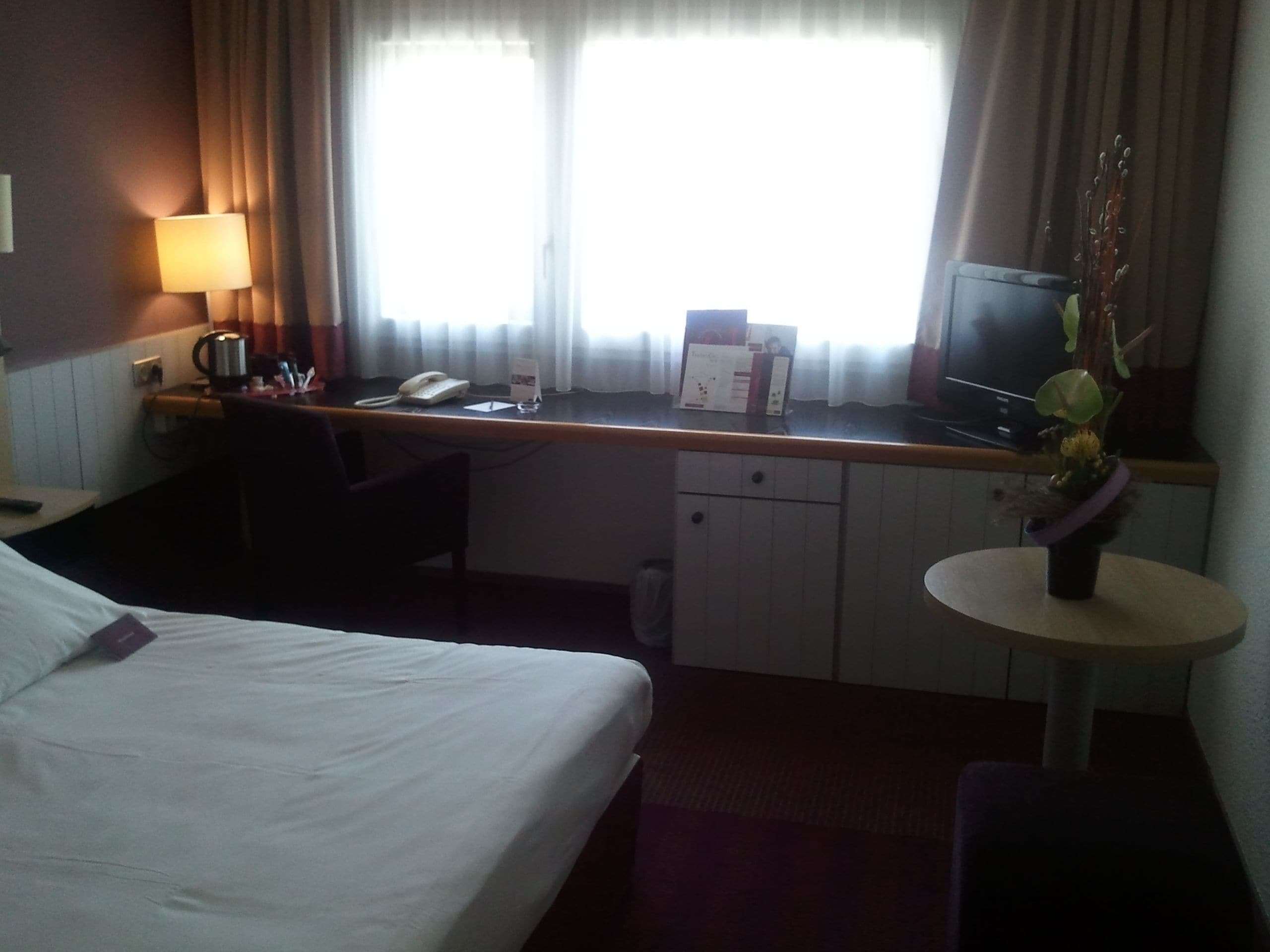 Una camera d'albergo con un letto, una scrivania, una sedia e un piccolo tavolino con un vaso.
