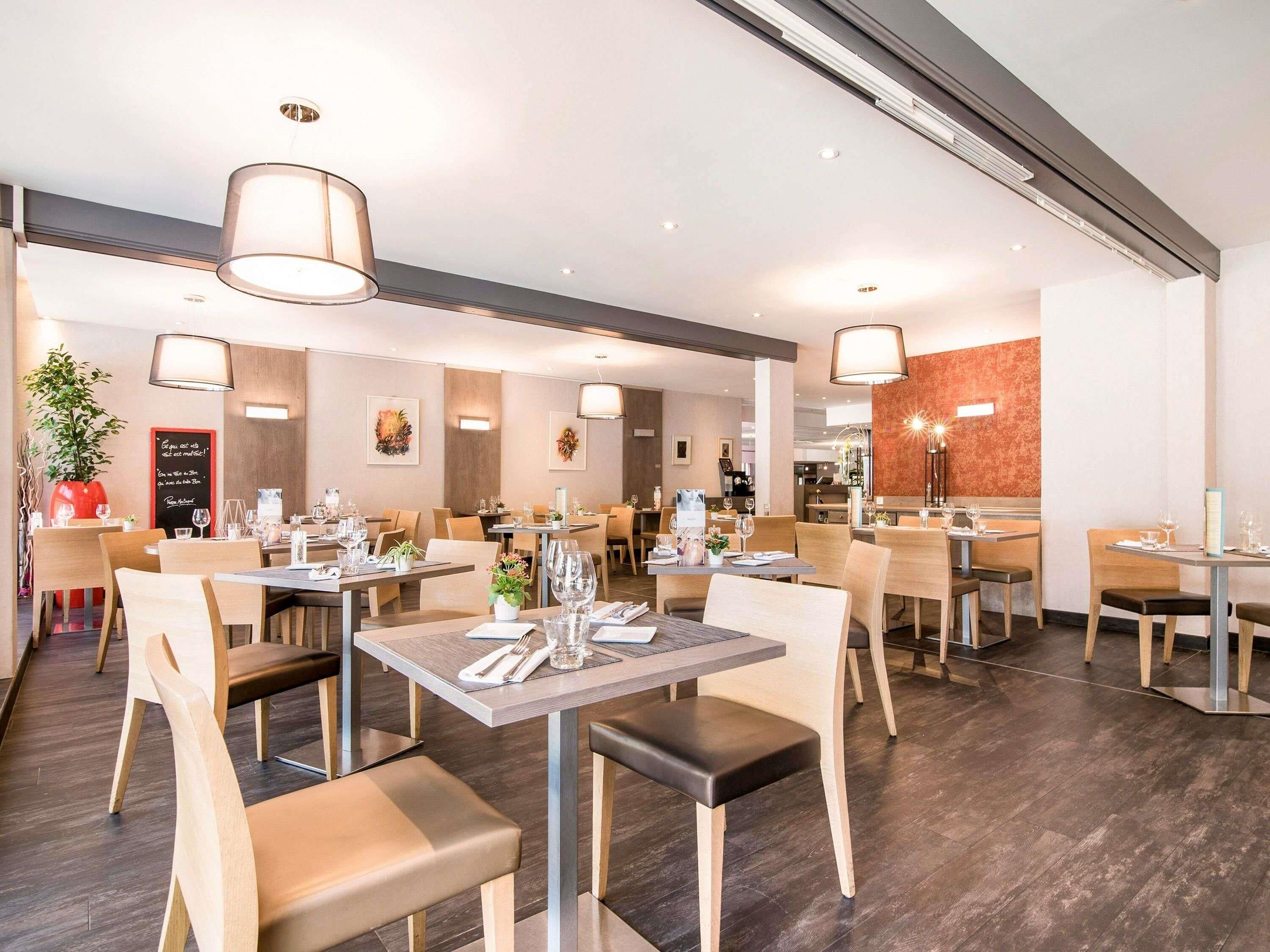 A modern restaurant interior with multiple dining tables and chairs, ambient lighting, and a clean, organized layout.