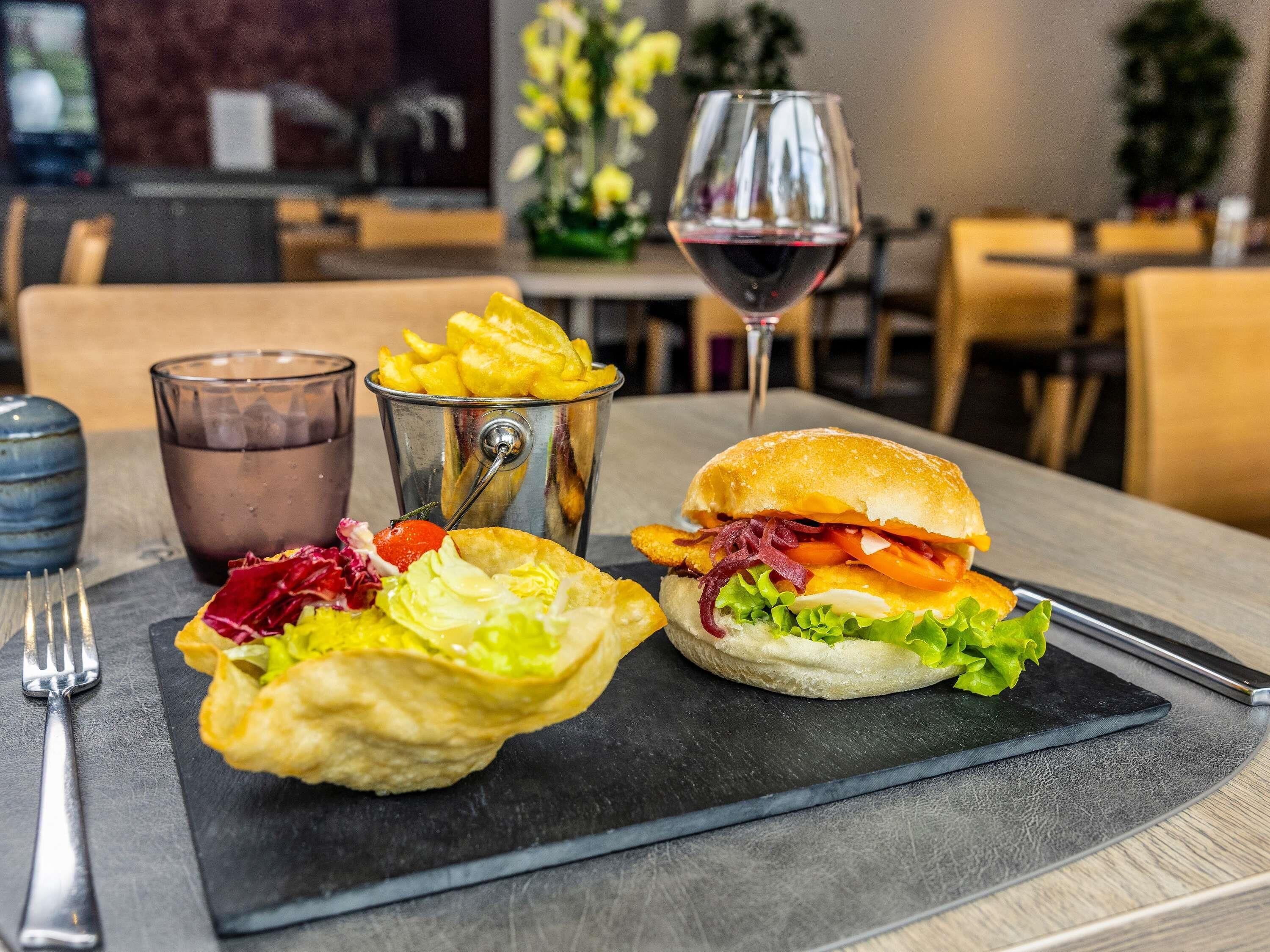 A dining table with a burger, fries, a glass of red wine, and a salad.