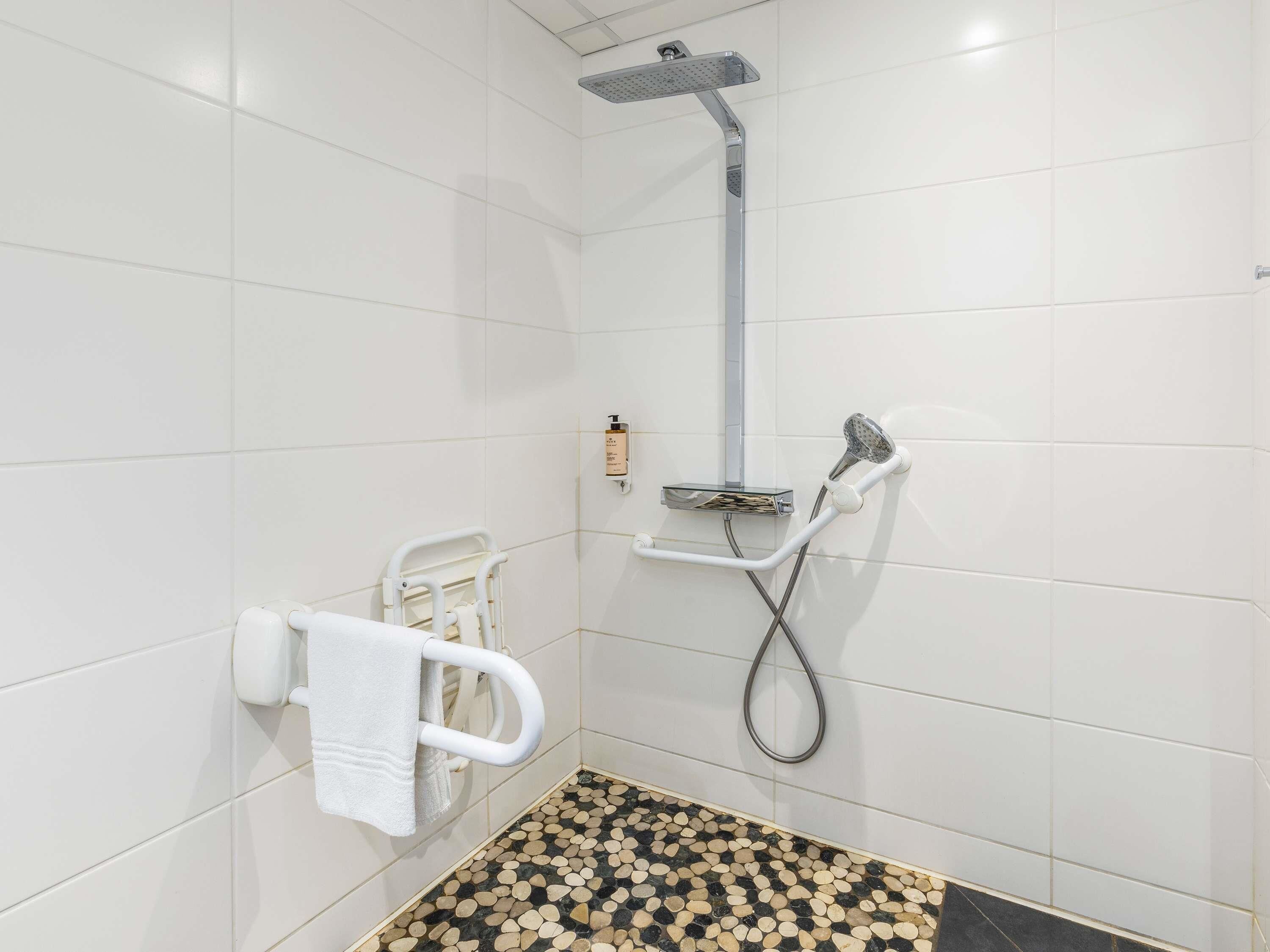 A shower area with a handheld showerhead, a wall-mounted soap dispenser, and a white grab bar.