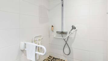 A shower area with a handheld showerhead, a wall-mounted soap dispenser, and a white grab bar.