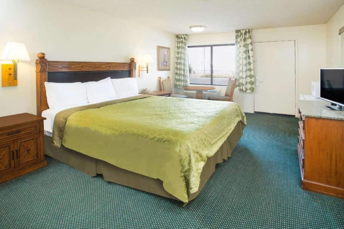 A hotel room with a bed, a television, a desk, and a window with curtains.