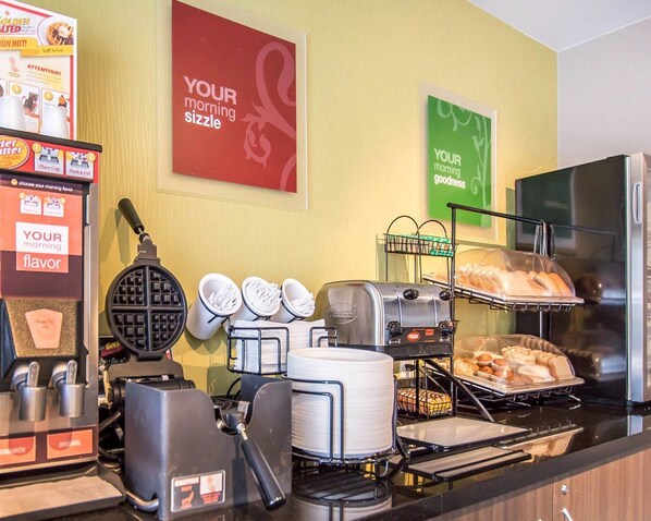 A breakfast station with waffle makers, a coffee machine, and trays of pastries.
