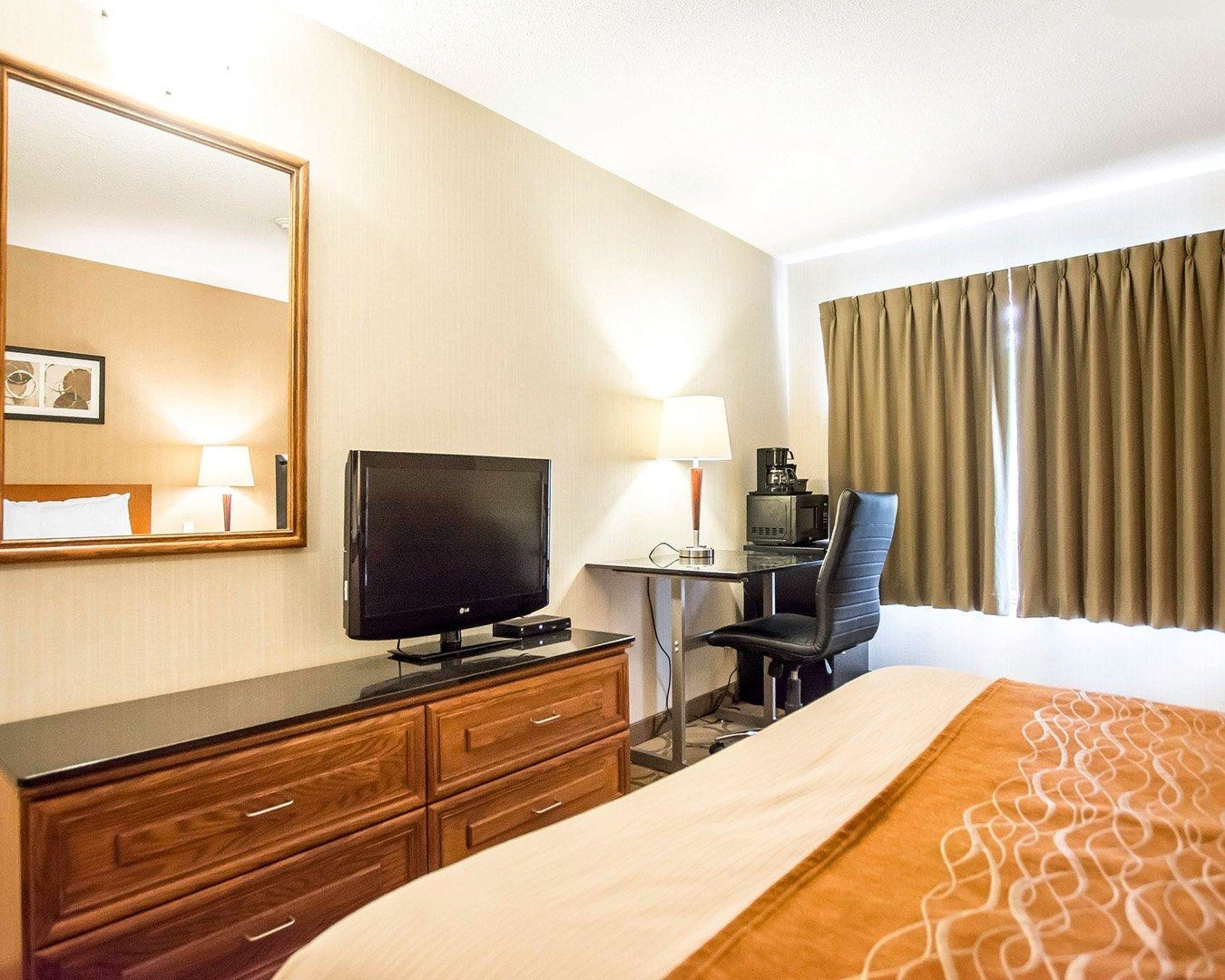 Une chambre d’hôtel avec un lit, un bureau avec un ordinateur, une télévision, une chaise et une fenêtre avec des rideaux.