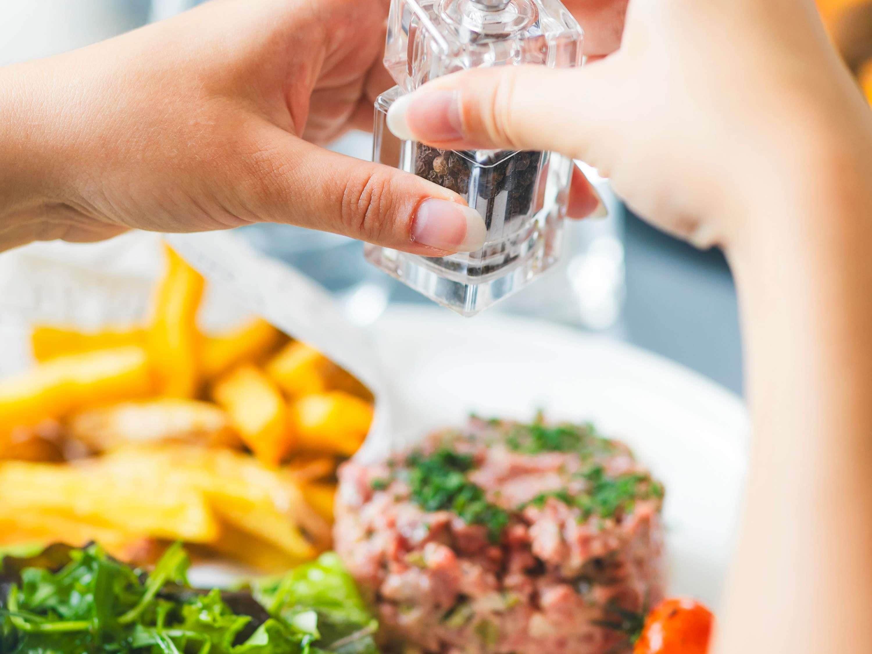 A person seasoning food with a salt shaker.