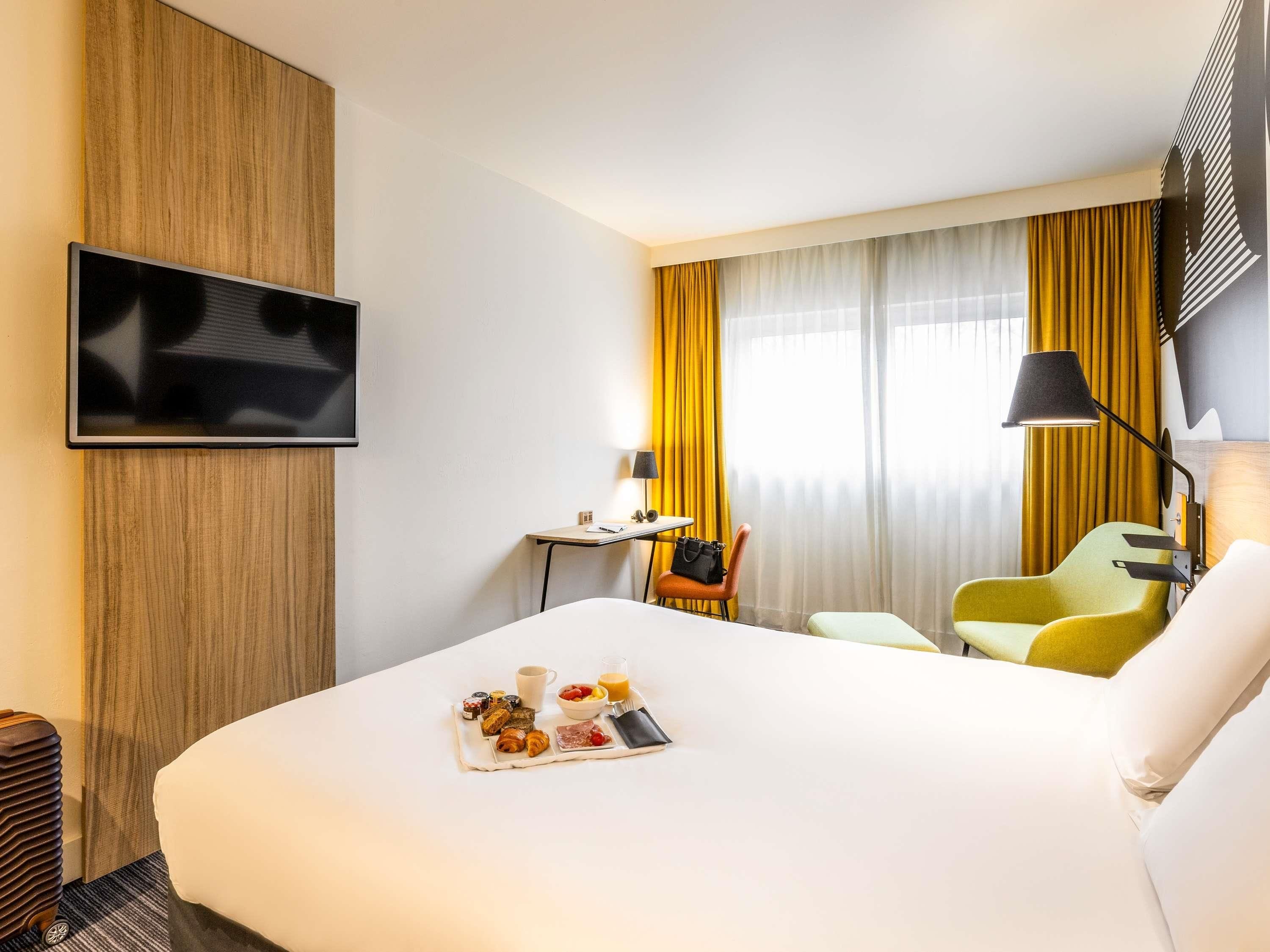 Une chambre d’hôtel équipée d’un lit, d’un bureau, d’une chaise, d’une télévision et d’un plateau de petit-déjeuner.