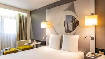 A hotel room with a bed, a desk, a chair, and a wall-mounted lamp.
