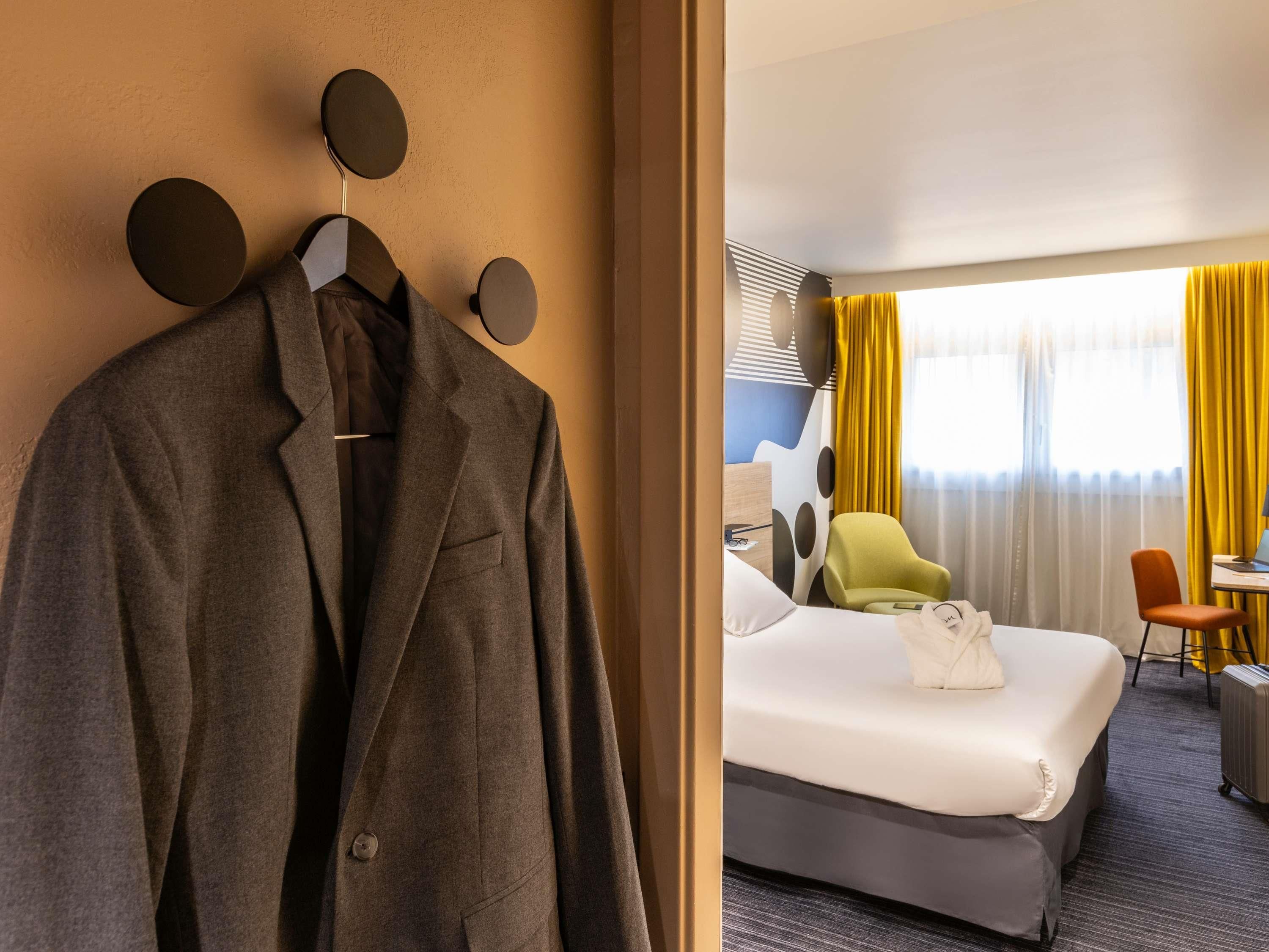 A hotel room with a bed, a desk, a chair, and a coat rack with a suit.