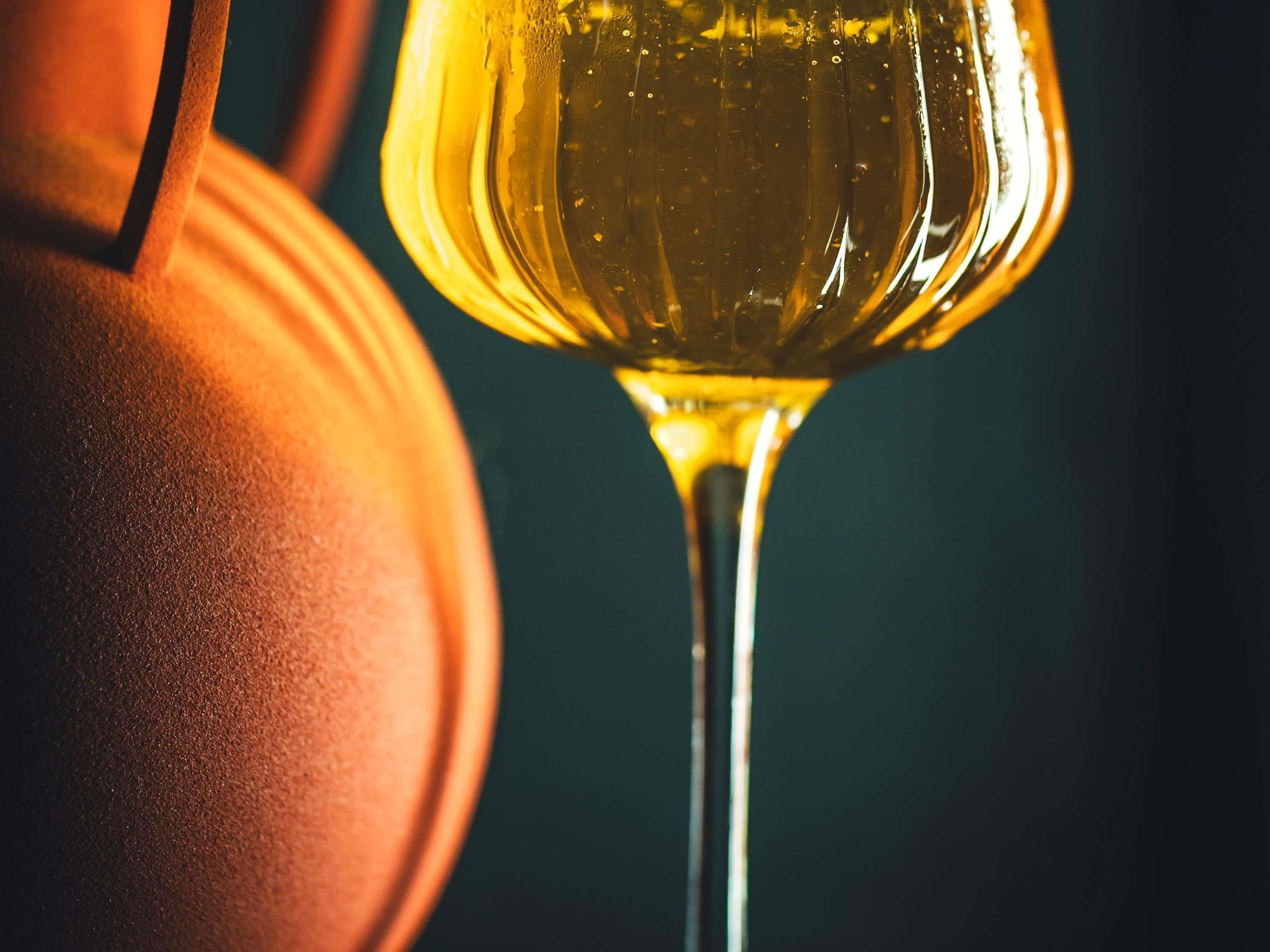 Primer plano de una copa de vino con un líquido transparente, posiblemente vino, y un objeto oscuro y texturizado a su lado.