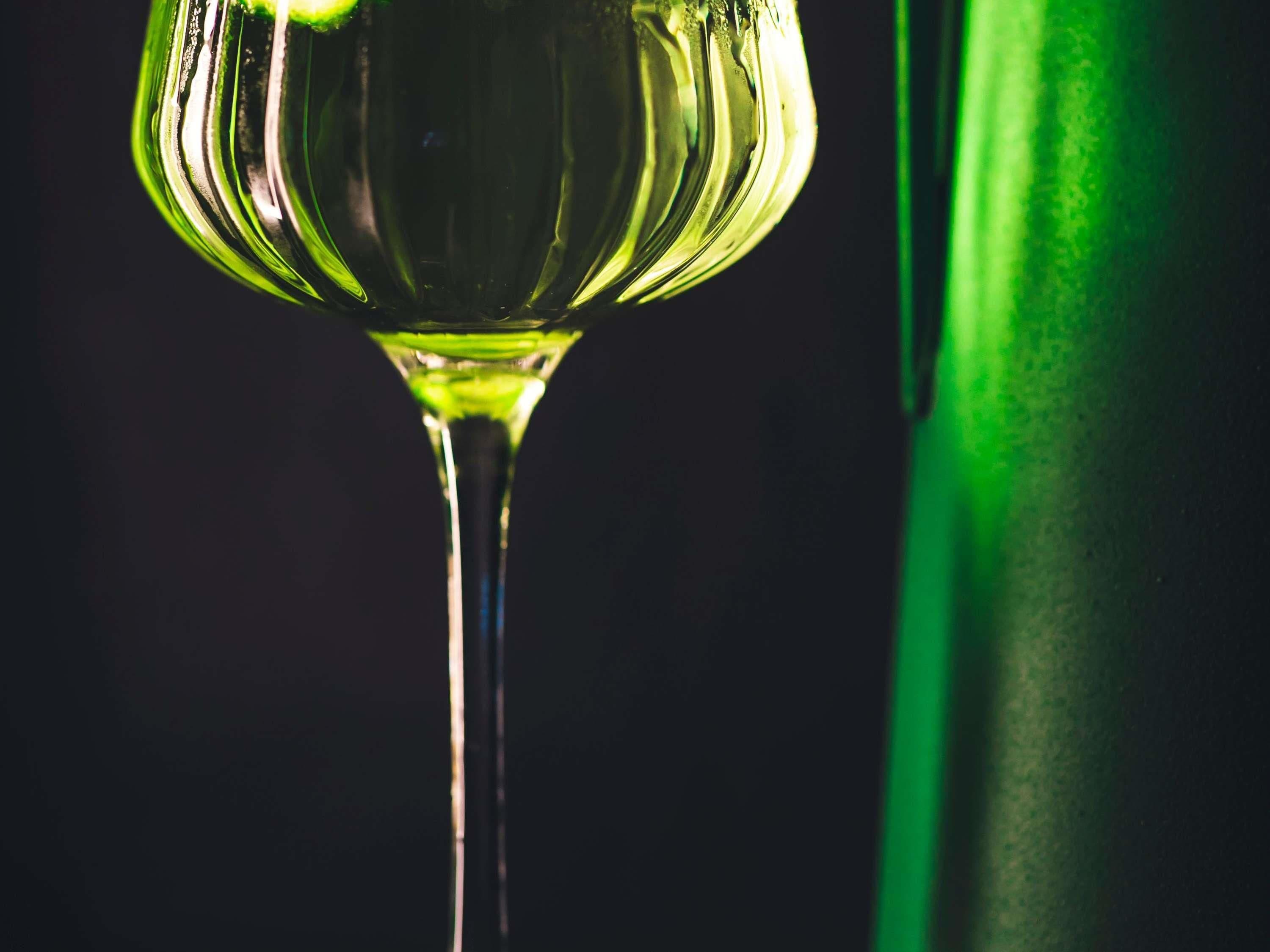 Un gros plan d’un verre à vin contenant un liquide vert, vraisemblablement du vin, sur un fond sombre.