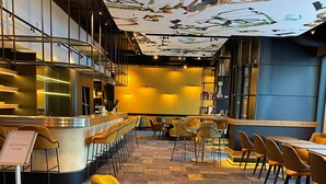 Un restaurante con zona de bar, diferentes disposiciones de asientos y un techo con diseño.