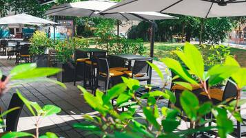 An outdoor seating area with tables and chairs, umbrellas, and greenery.