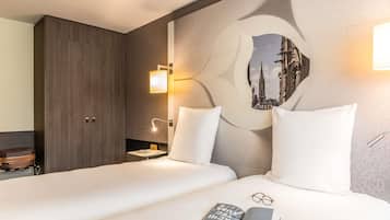 Une chambre d’hôtel avec un lit, des oreillers, une table de chevet, une lampe, un tableau accroché au mur et une valise.
