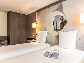 Une chambre d’hôtel avec un lit, des oreillers, une table de chevet, une lampe, un tableau accroché au mur et une valise.