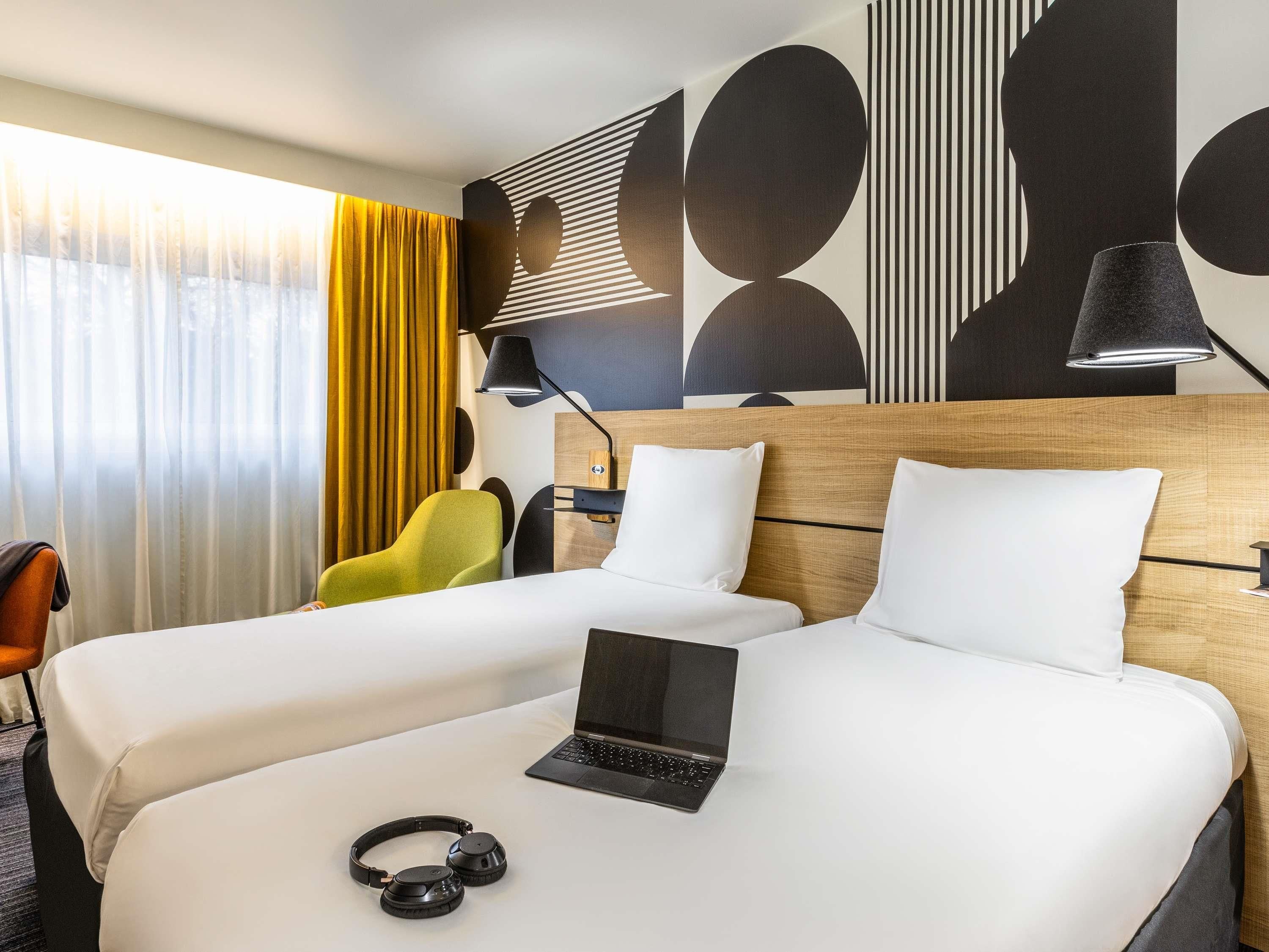 Een hotelkamer met twee bedden, een laptop, koptelefoon en een lamp.