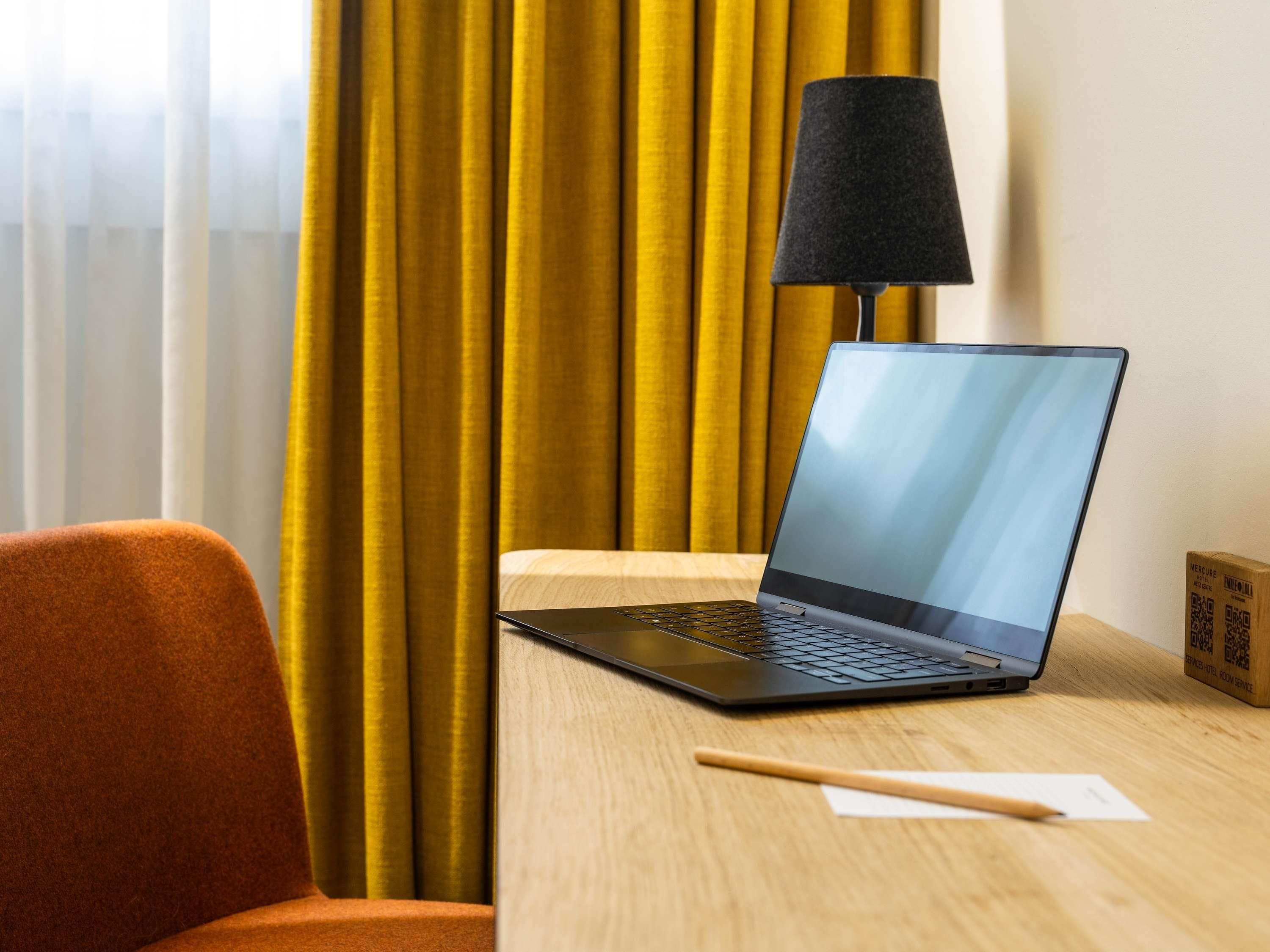 A laptop on a wooden desk with a black lamp, a pencil, and a small box with QR code.