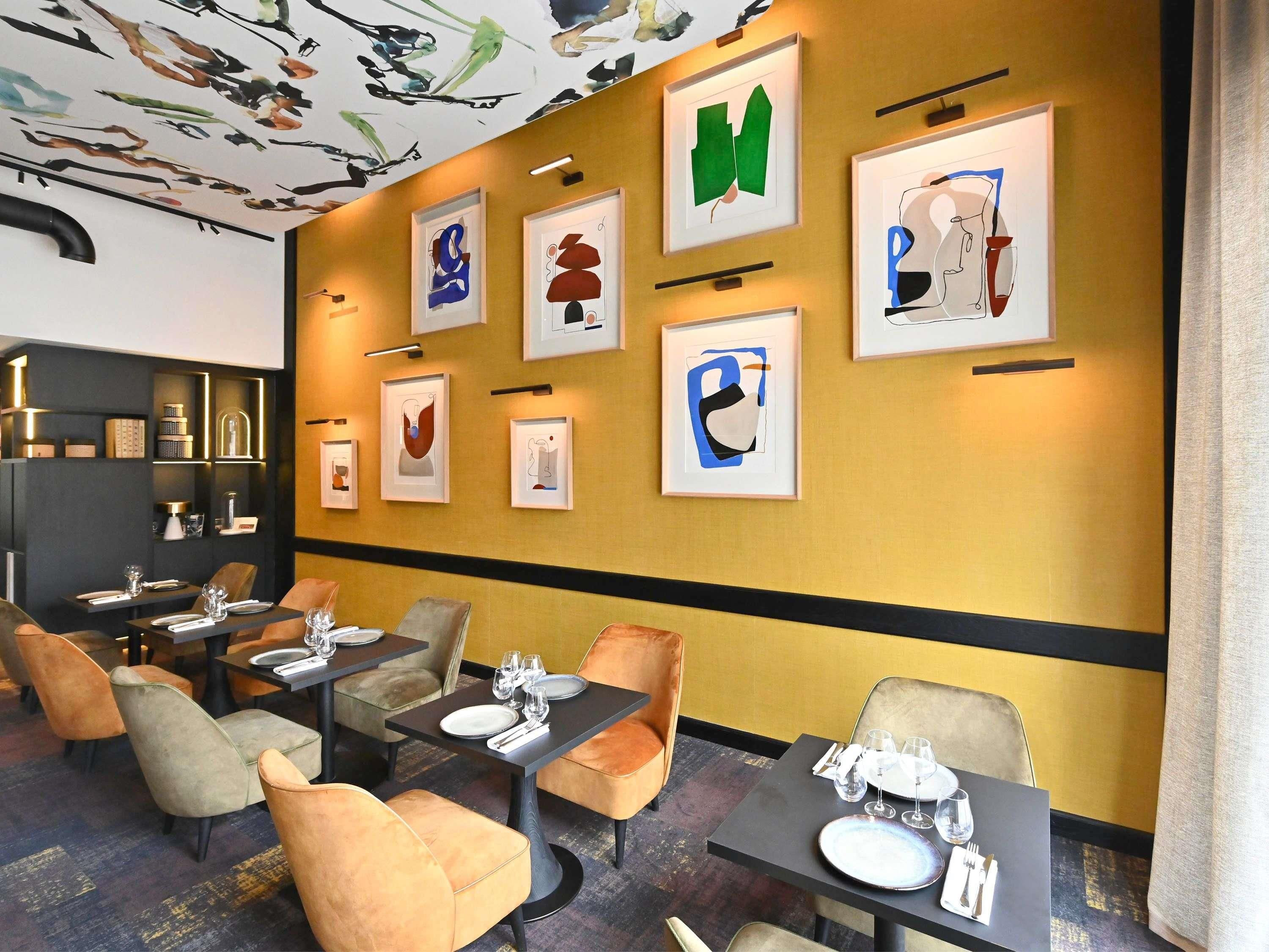 A restaurant with tables set for dining, framed artwork on the wall, and a ceiling with abstract designs.