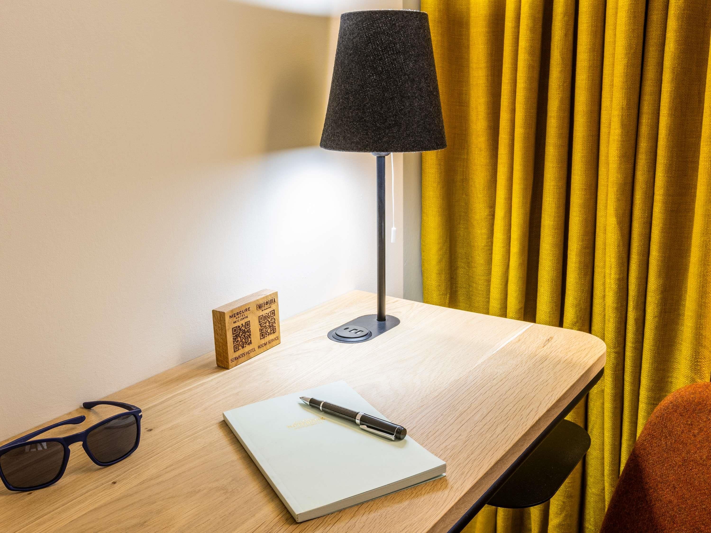 Un bureau en bois, une lampe, un bloc-notes, un stylo et une paire de lunettes de soleil.