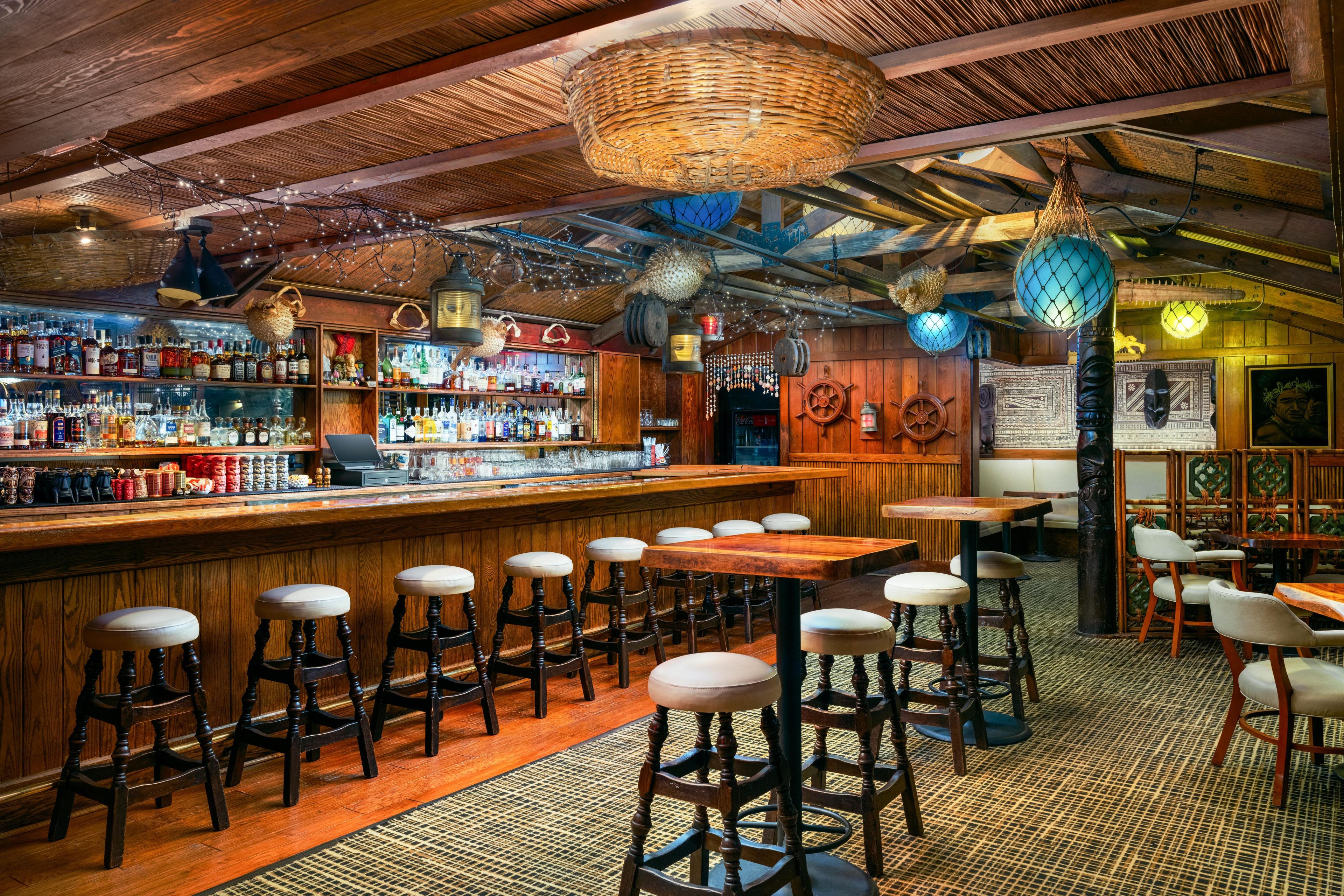 A bar with wooden stools, a bar counter stocked with bottles, and hanging decorations.