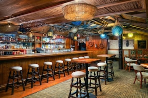 A bar with wooden stools, a bar counter stocked with bottles, and hanging decorations. - Hilton Atlanta (Atlanta)