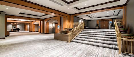 A spacious hotel lobby with a grand staircase, multiple doors, and a piano.