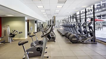 Ein Fitnessraum mit mehreren Laufbändern und Ergometer, einer Uhr und einem Fenster mit Blick nach draußen.