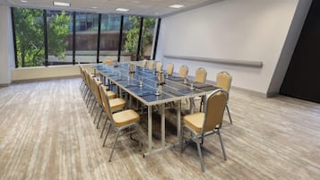 A conference room with a long table, chairs, and a view of greenery outside.