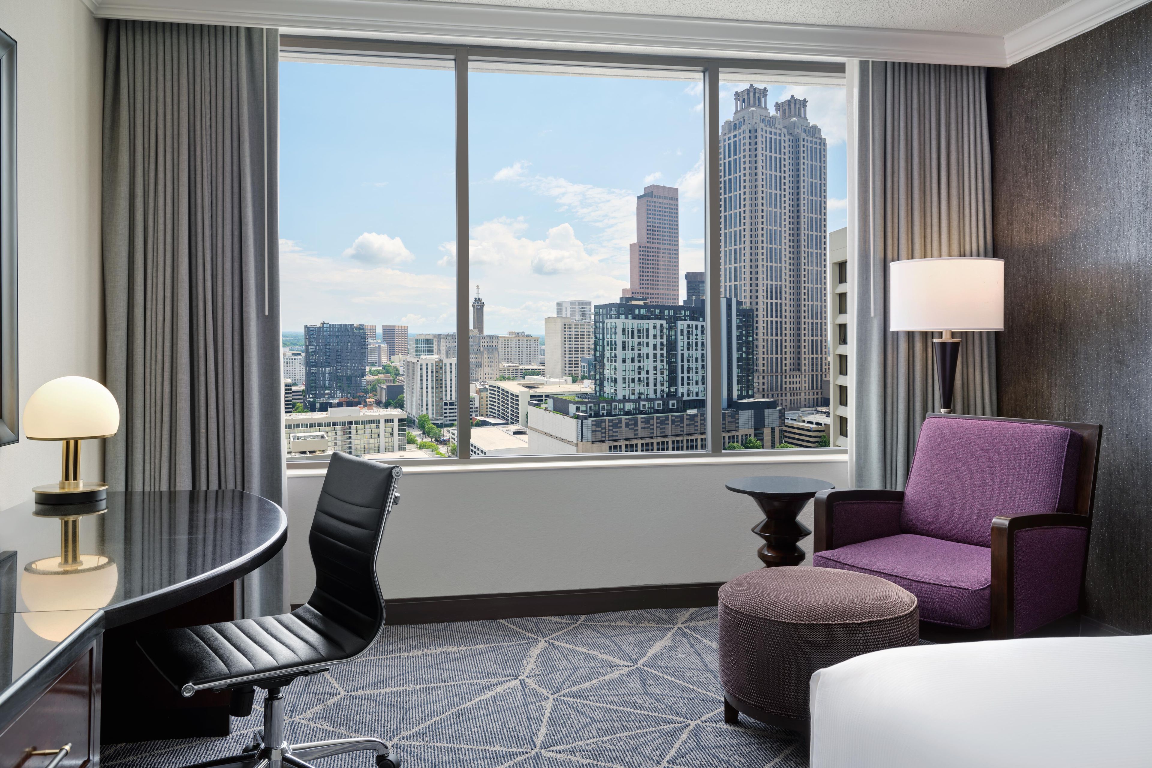 Une chambre d’hôtel avec vue sur la ville, un bureau, une chaise, un canapé et une lampe.