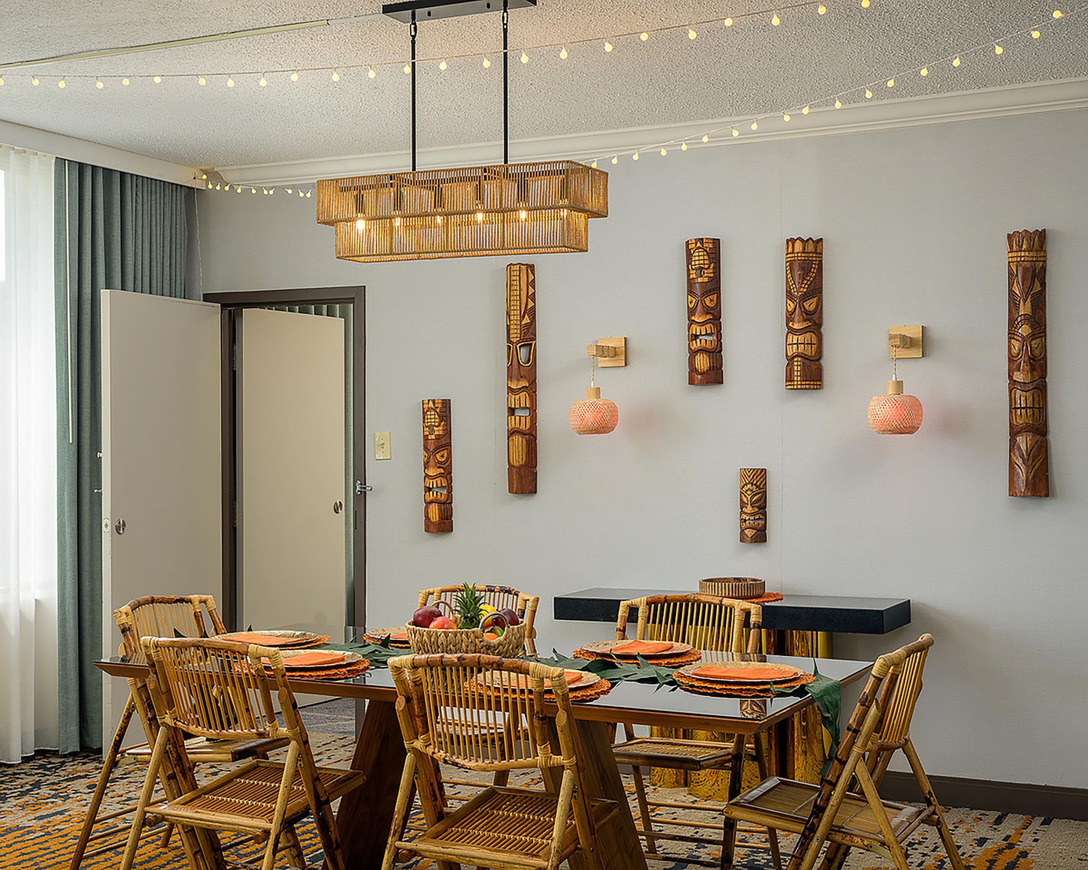 A dining area with a table set for four, surrounded by wicker chairs, a hanging light fixture, and decorative wooden panels on the wall.