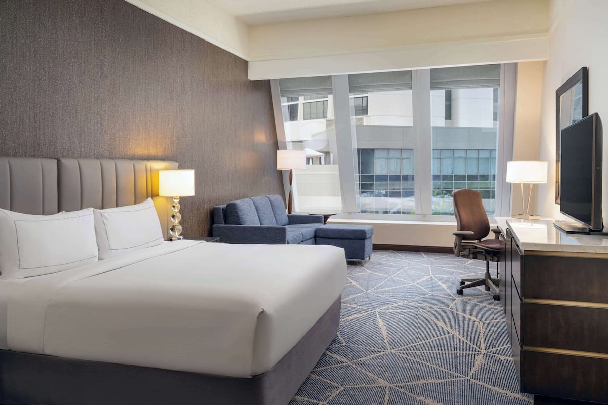 A hotel room with a large bed, a sofa, a desk with a chair, and a TV.