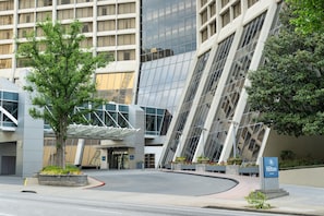A modern hotel entrance with a glass facade, a covered walkway, and a landscaped area with planters.