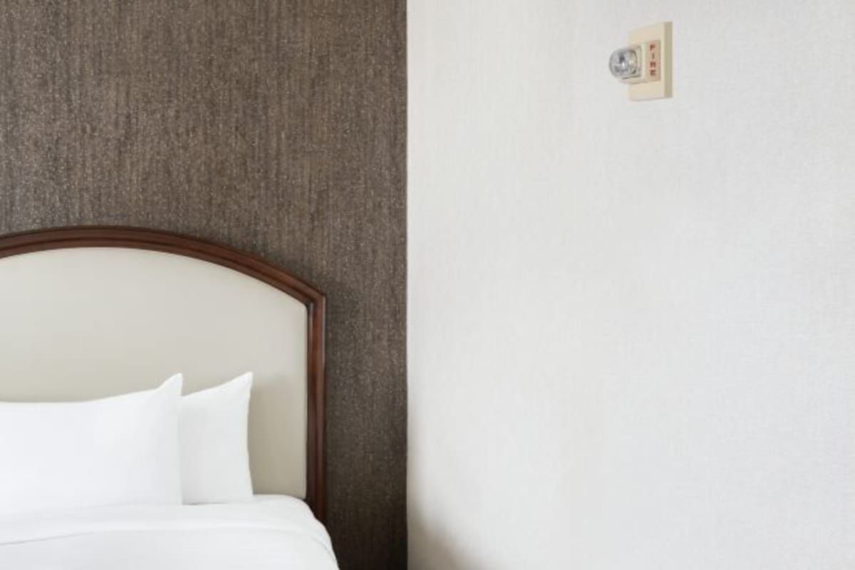 A hotel room with a bed against a textured wall and a light switch on the wall.