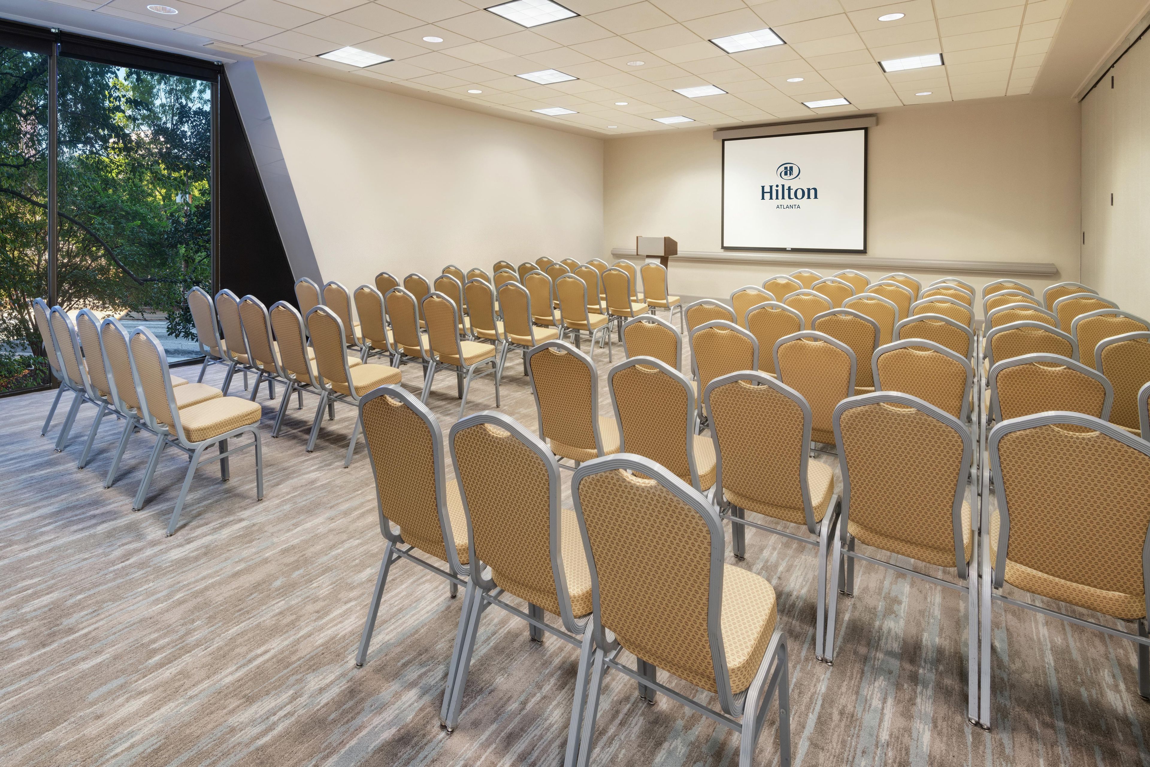 A conference room with rows of chairs, a projector screen, and a presentation area.