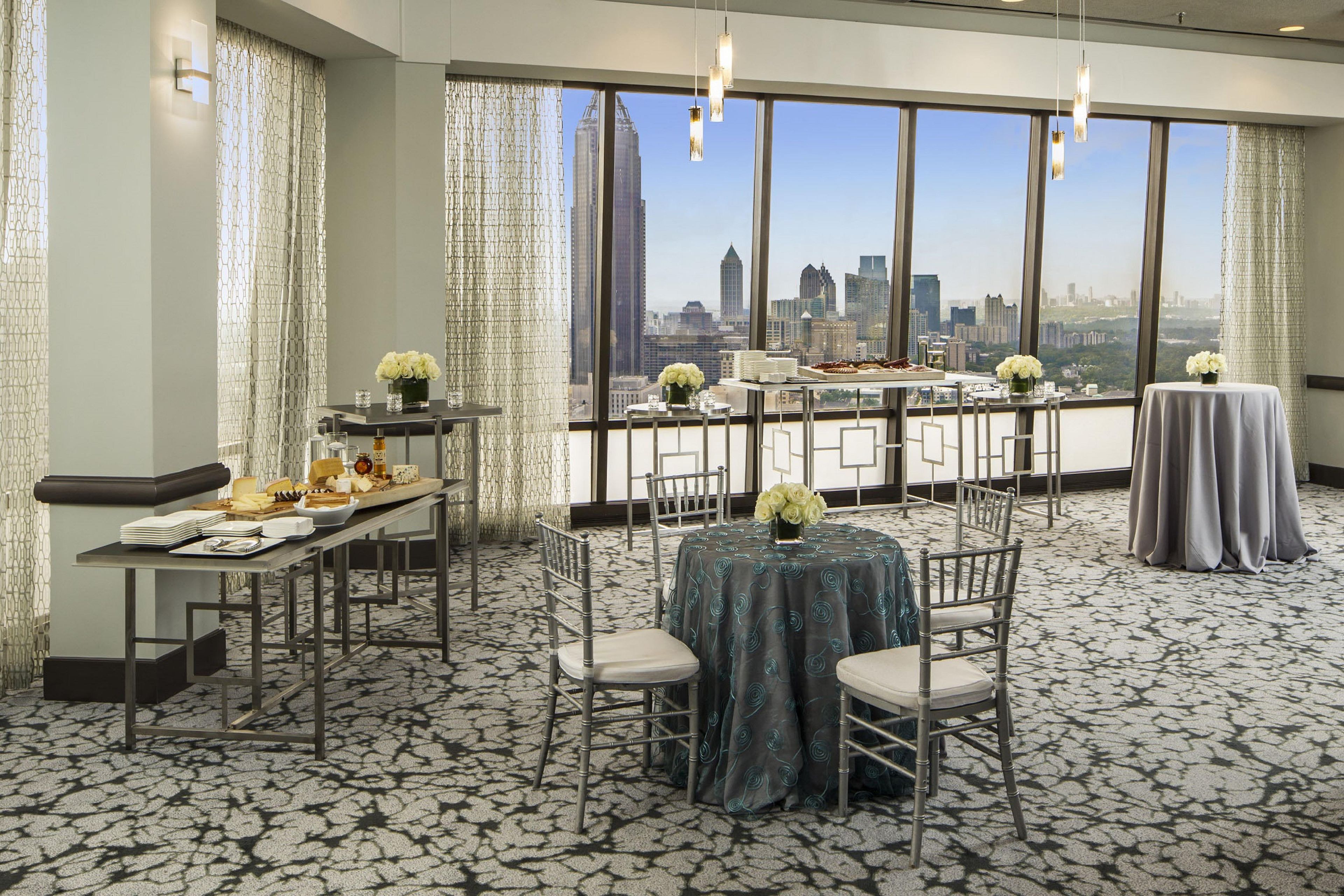 A hotel room with a city view, a dining area with tables and chairs, and a balcony with a table set for a meal.