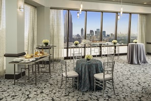 A hotel room with a city view, a dining area with tables and chairs, and a balcony with a table set for a meal.
