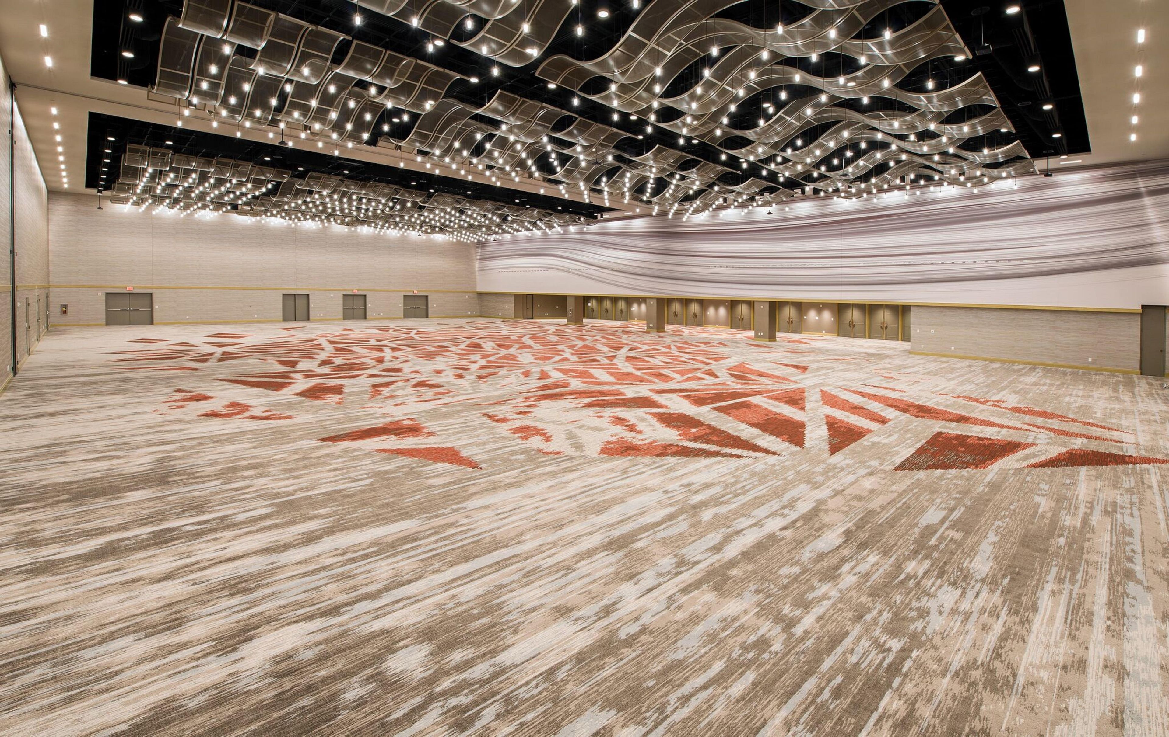 A spacious indoor area with a patterned carpet, a high ceiling with hanging lights, and a row of doors along the wall.